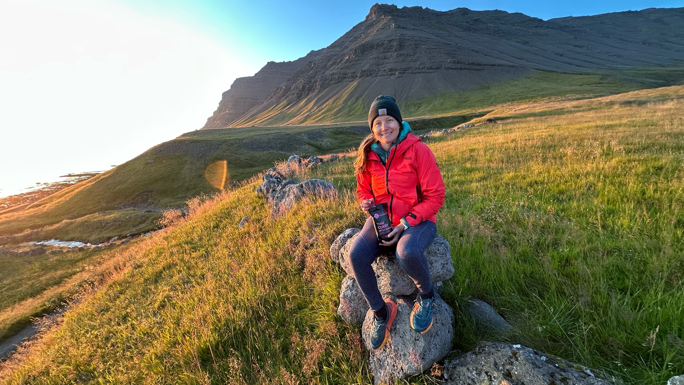 Tester sits on rock on windy outcropping in Iceland wearing Columbia Saudan Pro rain shell